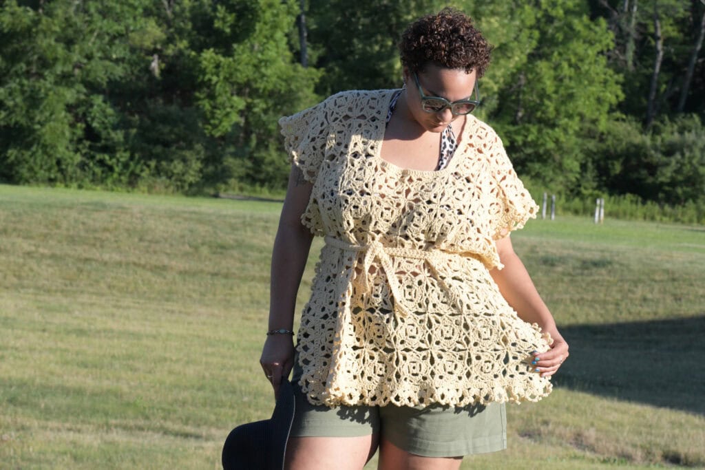 Lightweight crochet top with airy stitch detail, worn outdoors; textured yoke and sleeves shown for summer layering ideas.