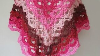 Triangular crochet shawl with open lace stitches and a gradient from deep red to light pink, shown on a mannequin.