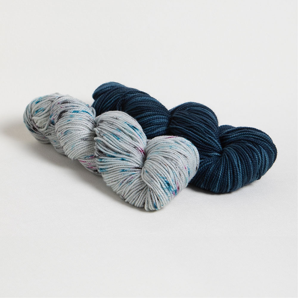 Three skeins of Hawthorne DK yarn are neatly arranged on a white surface. The yarns include two shades of gray with speckles of color and one in a deep navy blue. The textures appear soft and plush, ideal for knitting or crocheting projects like an Appalachian Cozy Up or a thigh-high knit sock pattern. -Marly Bird