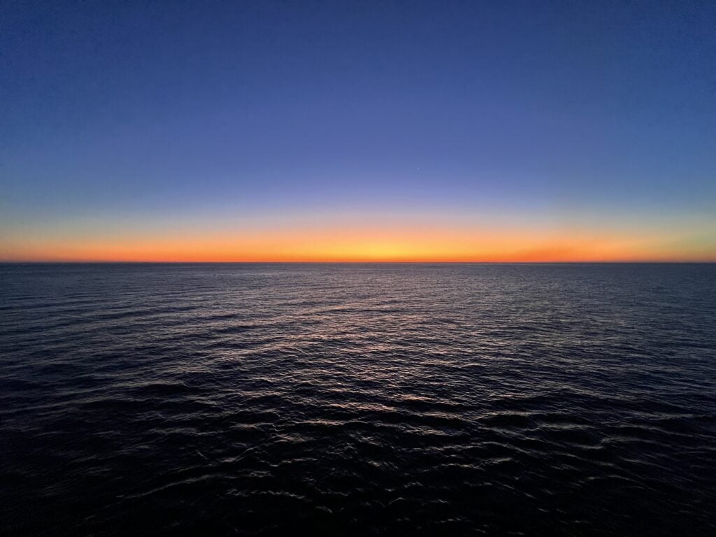 A crochet blanket with wave patterns in orange, yellow, and blue yarns, mimicking a serene sunset ocean horizon.