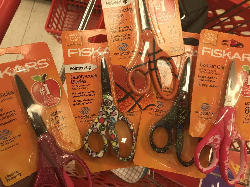 child safety scissors are great for knitters who travel because they are safe to bring in your carry on luggage - image is of a pile of scissors in a basket during back to school supply shopping - Marly Bird 
