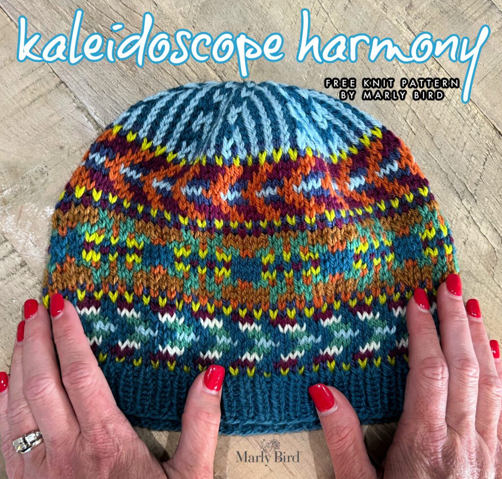 The image captures a hand-knit hat with an intricate colorwork pattern, being held by a pair of hands with red nail polish. The hat is richly colored with a variety of hues, forming a pattern that resembles a kaleidoscope. The ribbed brim of the hat is in a solid teal color, which transitions into the vibrant colorwork. Overlaying the image at the top is the text "kaleidoscope harmony," followed by "free knit pattern by Marly Bird," suggesting that this is a promotional image for a free knitting pattern offered by Marly Bird. The style of the hat and the choice of colors reflect Marly Bird's signature aesthetic, known for its bold and colorful designs. - Marly Bird