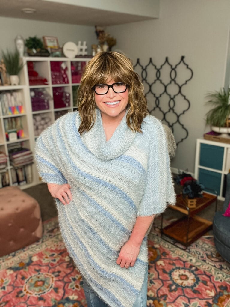 Person models a blue striped Woobie Poncho in a cozy room, showing off its knit texture and drape.