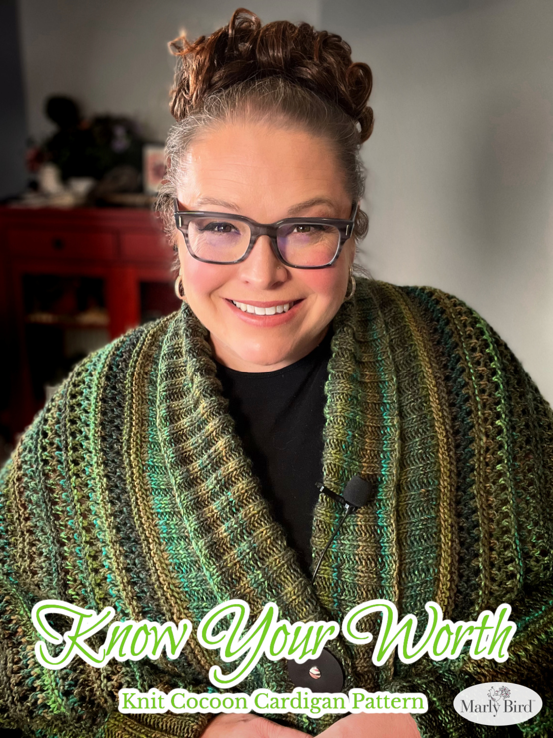 An elegantly draped, hand-knit cocoon cardigan displayed on a mannequin, showcasing rich hues of green with a subtle variegated pattern, a chunky ribbed collar, and a large decorative button at the front. Know Your Worth Knit Cocoon Cardigan Pattern by Marly Bird