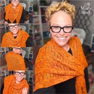 Woman with curly blonde hair wears an orange knit Lehabah Fire Sprite Shawl, showing lace detail; bookshelves in background.