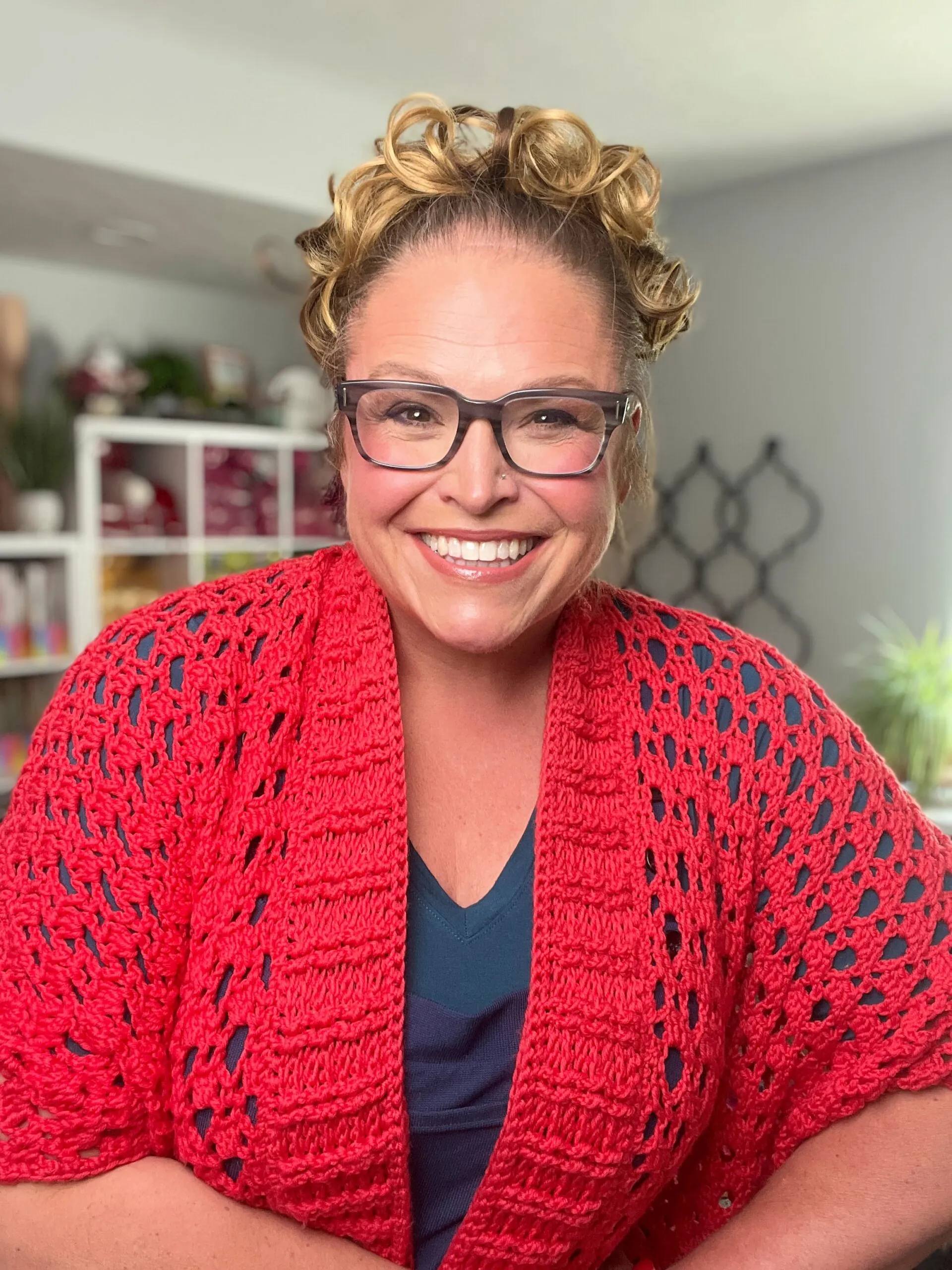 Bright red crochet ruana shawl with textured openwork stitch, draped over shoulders and styled with a navy shirt indoors.