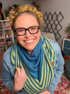 Person models a blue and yellow Tunisian crochet scarf with bold stripes, highlighting stitch texture and drape.