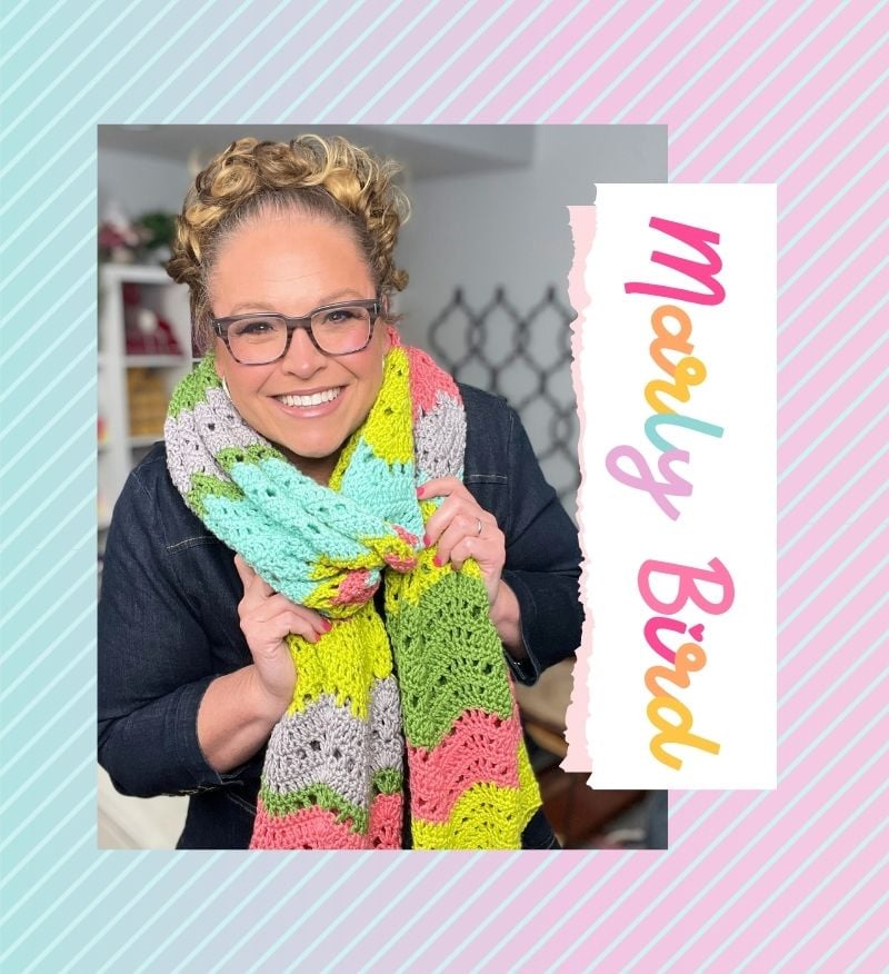 A woman with glasses and curly hair models a colorful crocheted scarf, showing textured stitches and vibrant yarn.