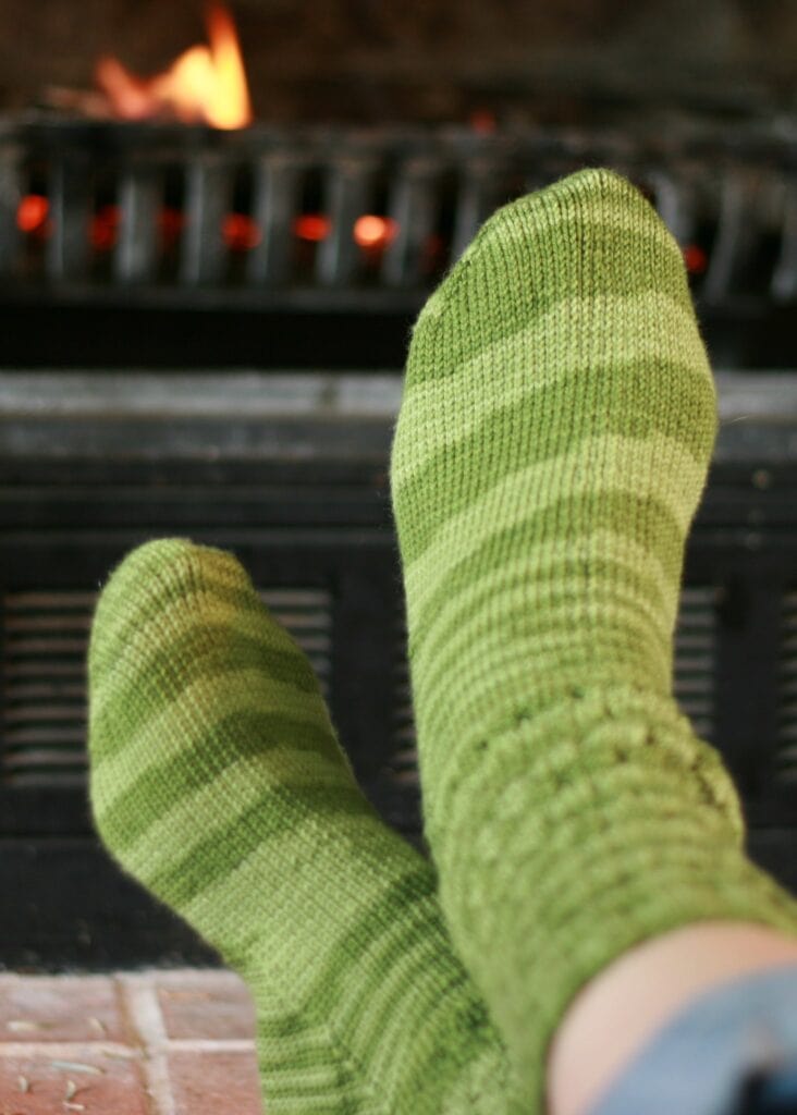 Green striped toe socks relaxing near a fireplace, cozy home comfort.