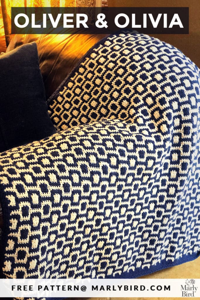 Navy and white geometric mosaic crochet baby blanket draped over a chair, highlighting texture and stitch detail