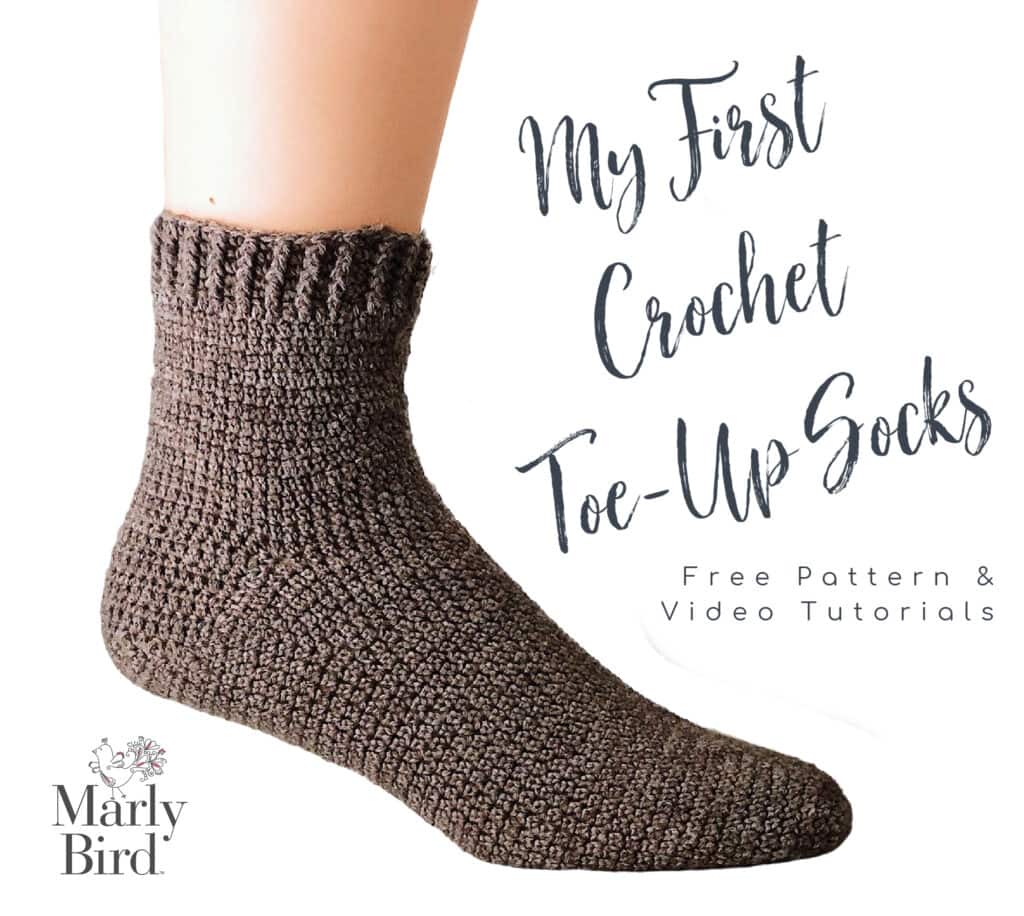 A close-up of a foot wearing a brown crochet sock labeled "My First Crochet Toe-Up Socks." Text also says "Free Pattern & Video Tutorials" with the Marly Bird logo in the bottom left corner. -Marly Bird