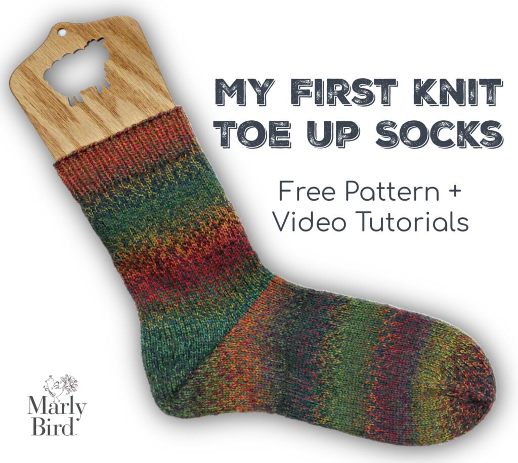 A colorful toe-up knit sock with a german short row heel is displayed on a wooden sock blocker. Marly Bird logo present.