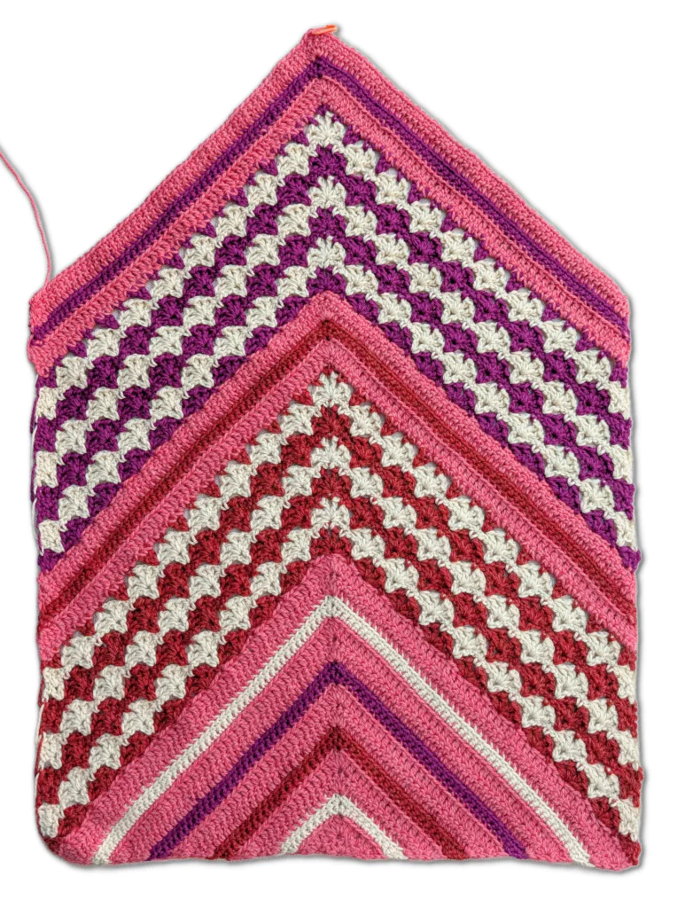 Chevron crochet fabric in pink, red, purple, and white yarn, displaying textured zigzag rows and a soft finish.