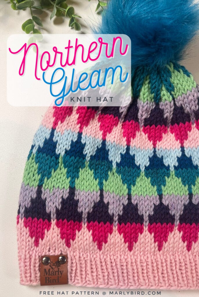 A colorful knit hat with a blue pom-pom, featuring diamond patterns in pink, blue, green, and purple. Text reads "Northern Gleam Knit Hat" and "One-day colorwork knit hat pattern @ marlybird.com." A Marly Bird tag is on the brim. -Marly Bird