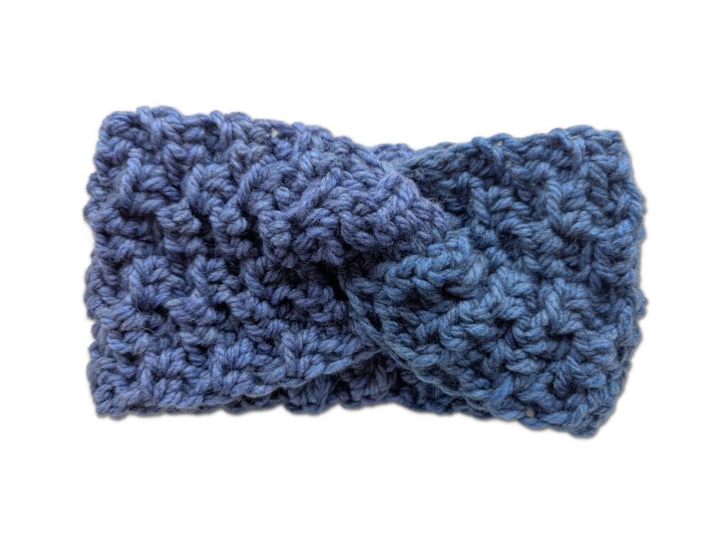 A close-up of a textured blue crochet headband with a twisted knot design in the center, set against a plain white background. -Marly Bird