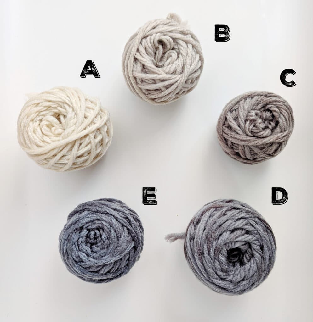 Five balls of yarn labeled A to E on a white background, perfect for crafting One Ball Wonders or a cozy Granny Square. A: cream, B: light beige, C: medium gray, D: dark gray, E: blue-gray. Ideal hues for creating an iPad Cozy with character and charm. -Marly Bird