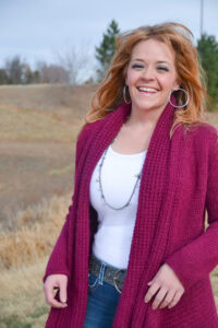 A woman in a maroon crocheted cardigan stands outdoors, showing detailed stitches and textured yarnwork.