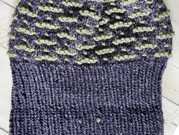 Knit fabric with a blue base and green textured pattern on top, featuring a ribbed section at the bottom. Small holes are visible in the lower part against a light wooden surface background, making it perfect for Game Day fashion in 2025. -Marly Bird