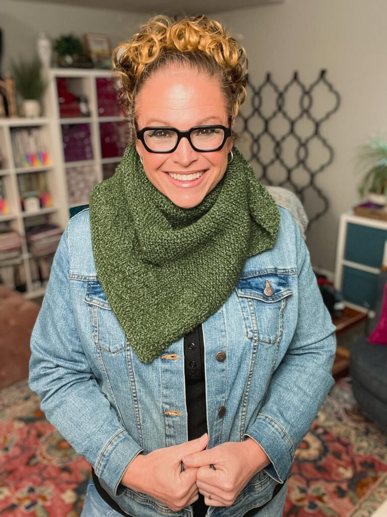 A woman models a green knit shawl with textured stitches, showing how the single-ball project drapes over a denim jacket.