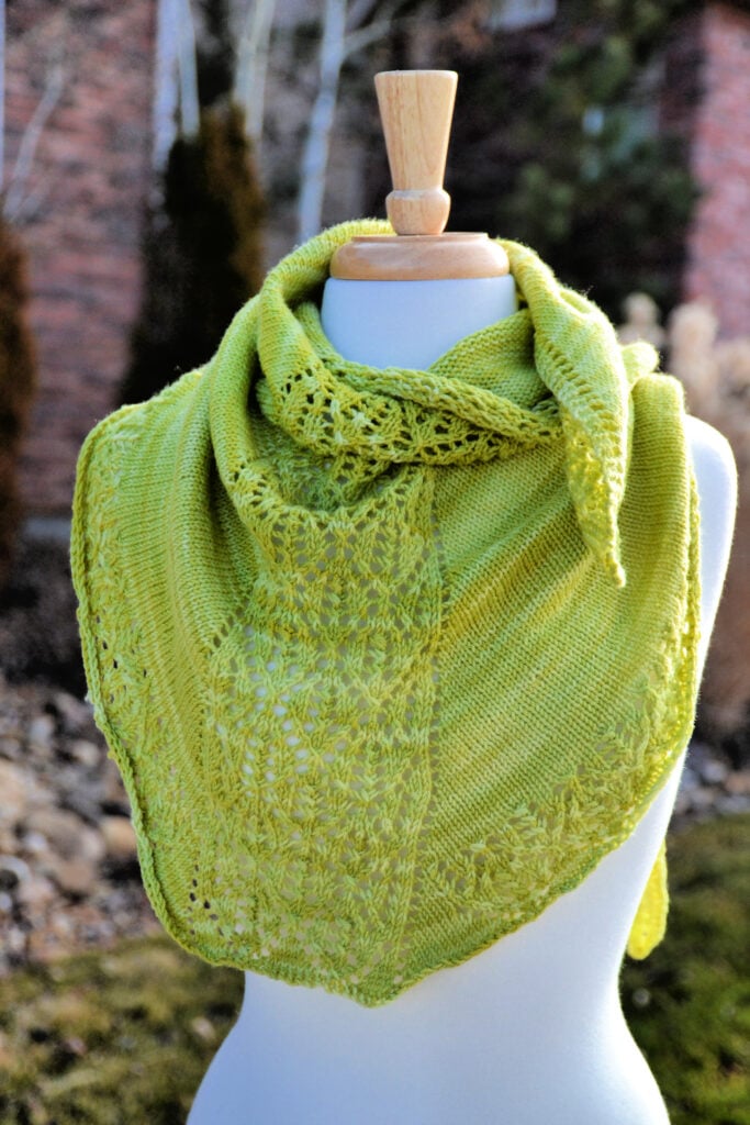 Pear Sorbet free knit lace shawlette in light green fingering weight yarn, displayed on a mannequin showing the lace center panel and stockinette body.