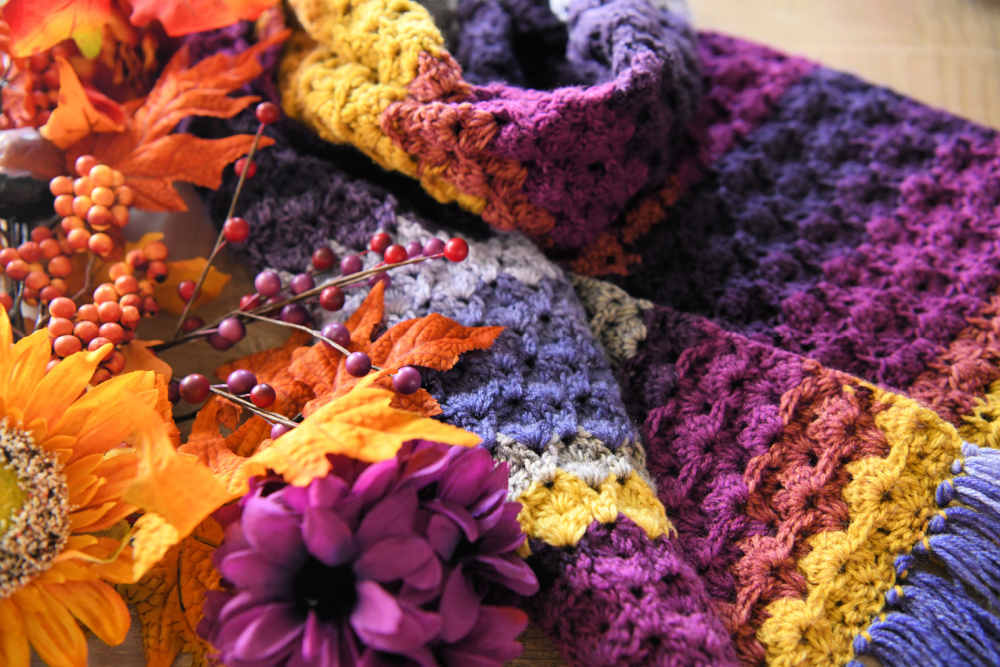 Petal Lace Scarf by Marly Bird on a wooden table with autumn foliage around it. 