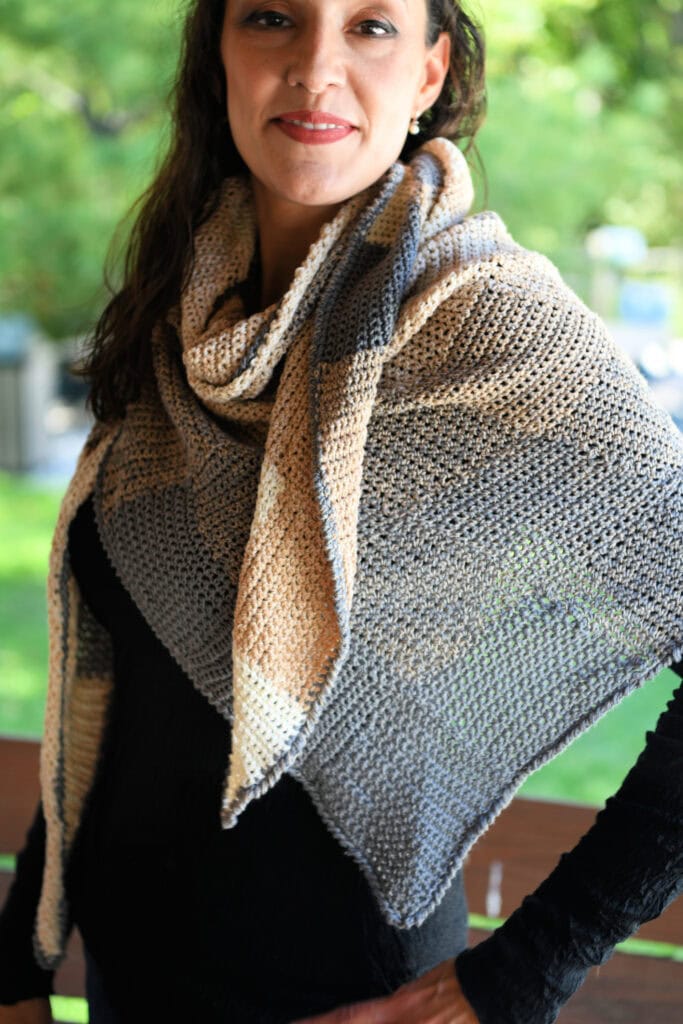 Woman outdoors models a crochet entrelac shawl in beige, gray, and blue with visible textured stitch blocks.