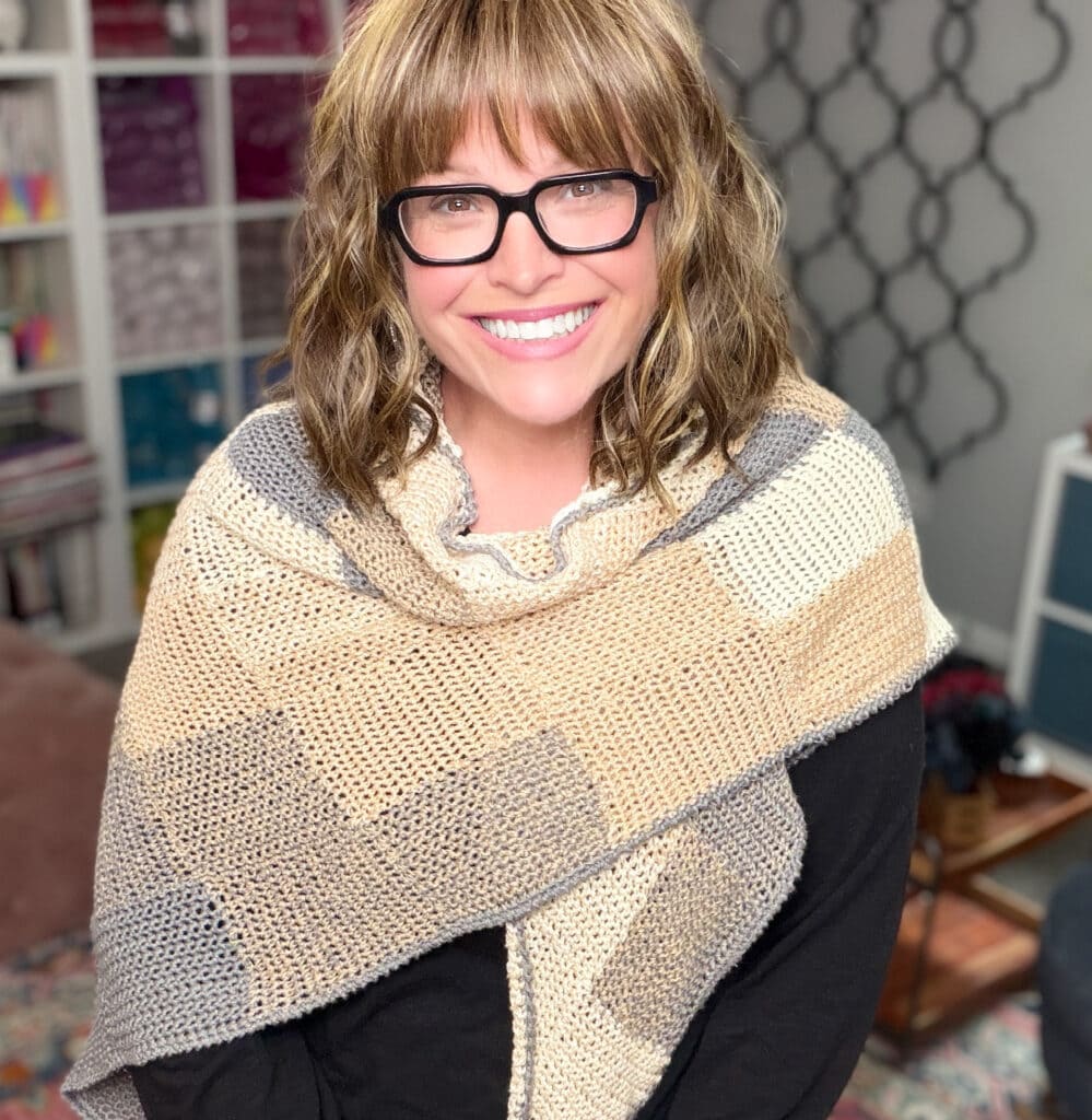 Woman models a beige and gray entrelac crochet wrap over a black top; textured stitches are clearly visible.