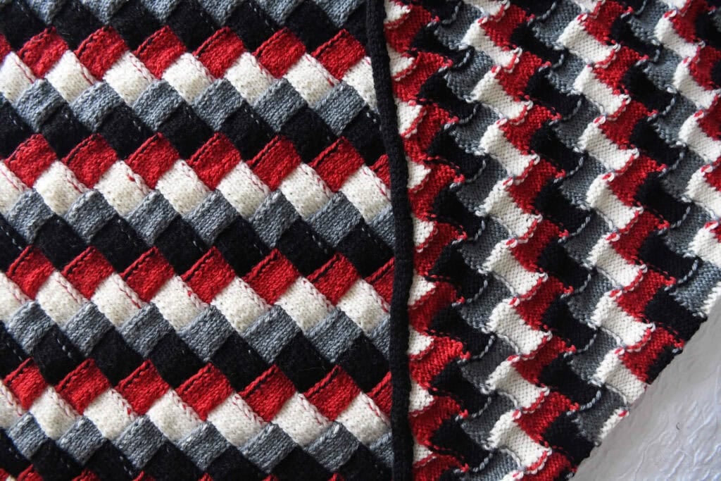 Close-up of two overlapping pieces of knitted fabric featuring a repeating diamond pattern in red, black, gray, and white. The texture and stitches are clearly visible, ideal inspiration for an entrelac knitting for babies project. -Marly Bird