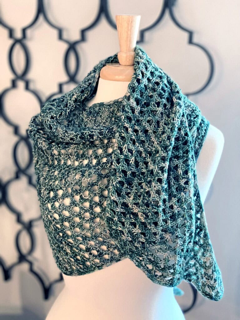 Light green crochet shawl with cable lace pattern, draped on a dress form; intricate texture shown against a cream backdrop.
