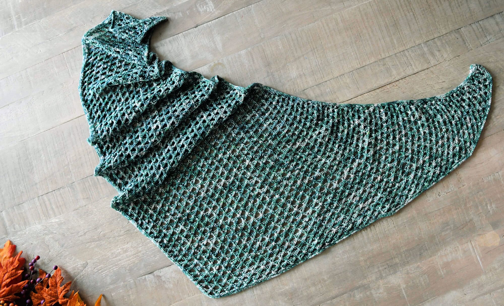 Crescent-shaped green and white shawl with cable and lace stitches displayed flat, textured stitches visible.