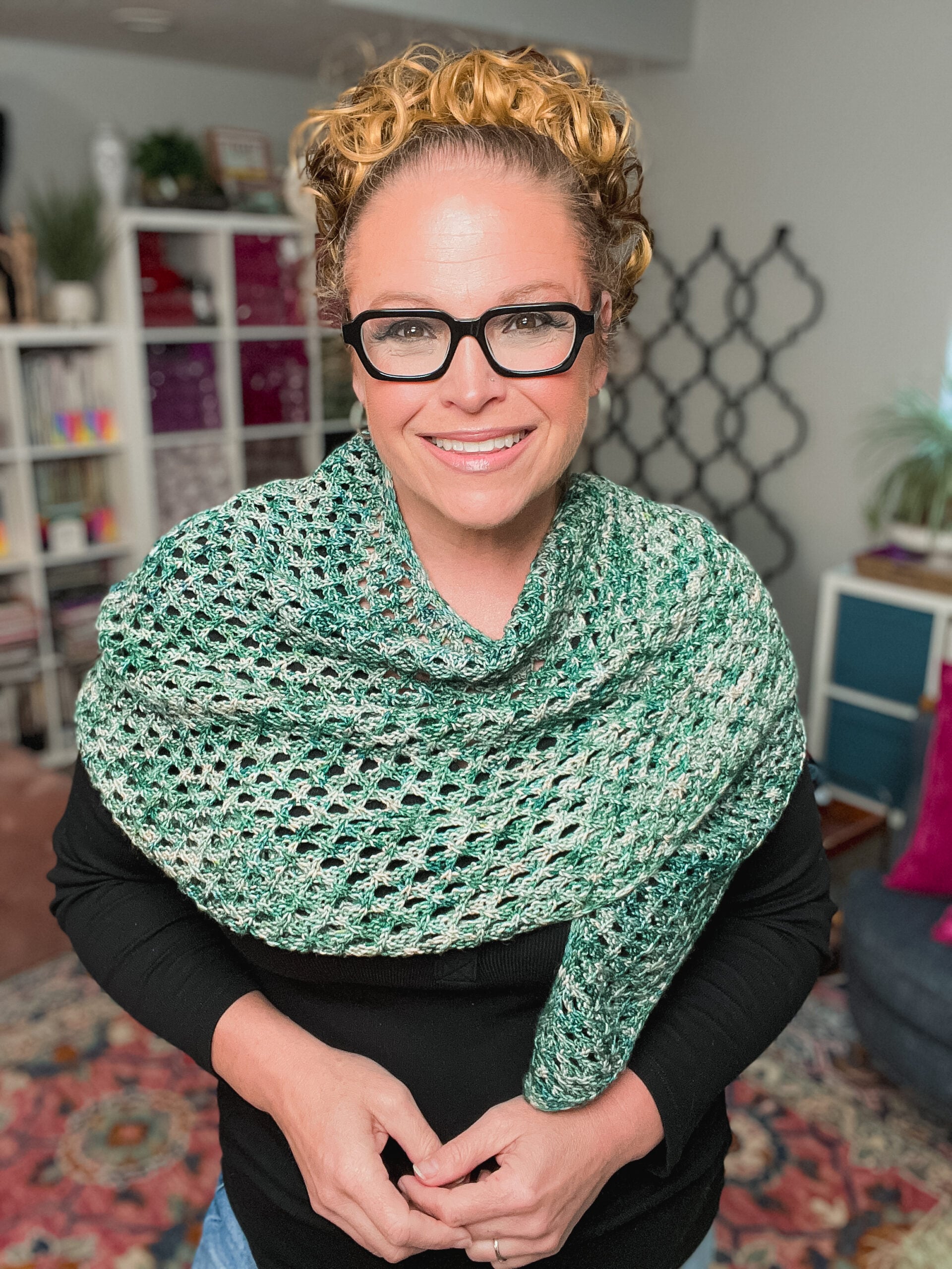 Green Boomerang Knit Shawl draped over shoulders, showing textured stitches and neat edges in a bright, creative space.
