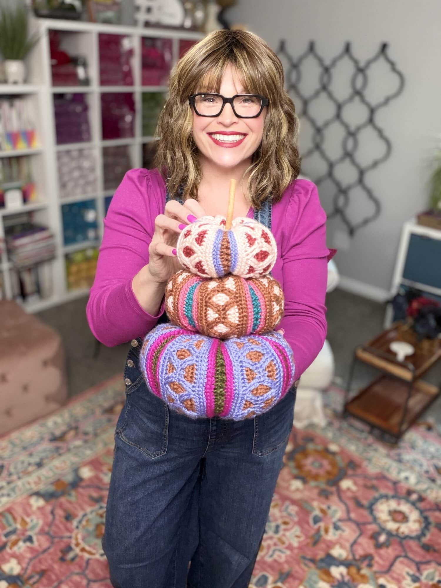 Marly Bird holding three stacked Rockford Mosaic Crochet Pumpkins in jewel-tone colorways