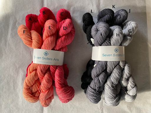 Bundles of Seven Sisters Arts yarn in various colors. On the left, shades range from red to coral and pink. On the right, shades vary from light gray to dark gray and black. Each bundle is neatly labeled with letters A to L. -Marly Bird