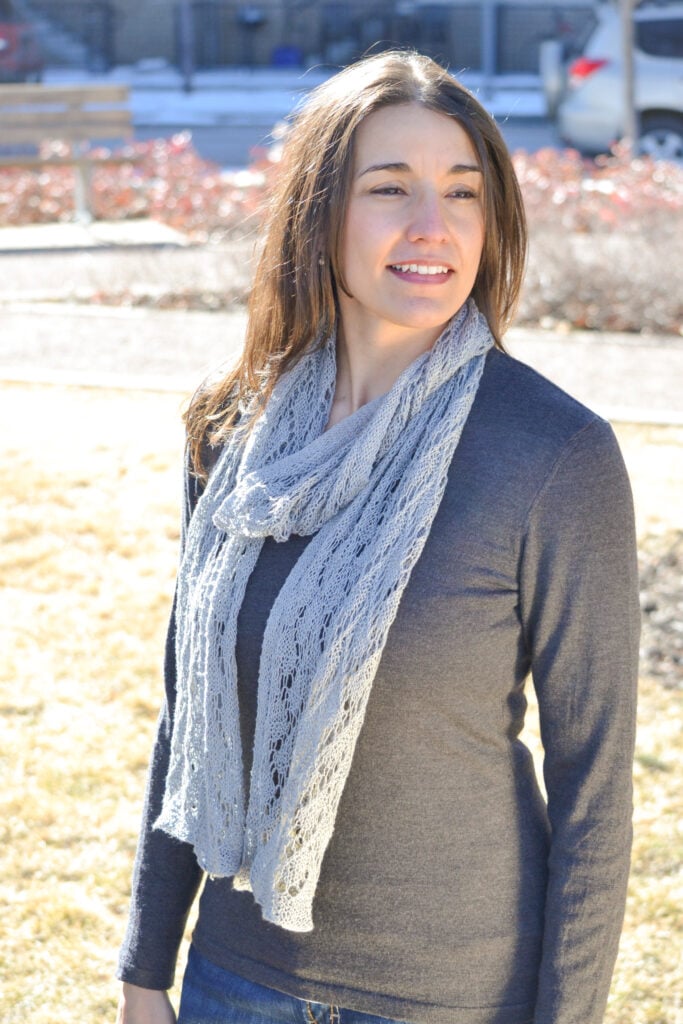Shangri-La free knit lace shawl scarf in light gray fingering weight yarn, draping over a dark top with delicate openwork stitches and texture clearly visible.