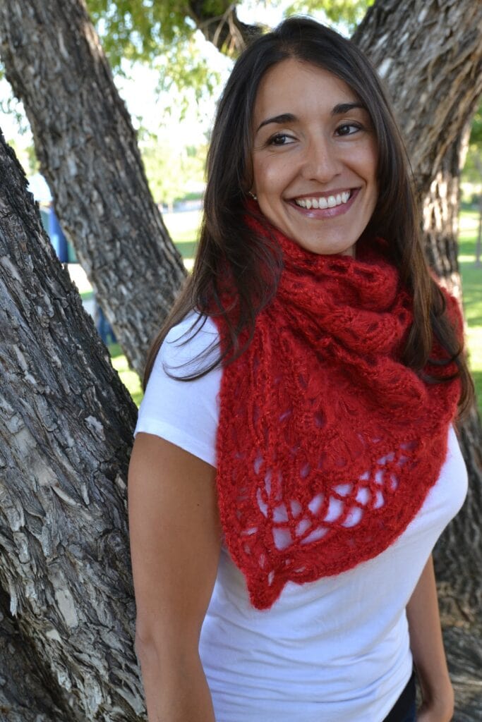 Woman outdoors wearing a red broomstick lace crochet scarf over a white tee; tree and grass background highlights scarf texture.