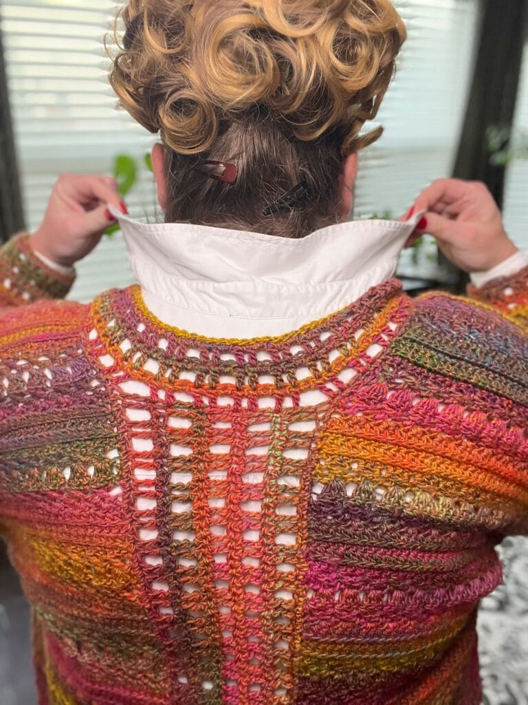 Colorful sookie crochet cardigan with textured stitches, worn over a white shirt; curly hair visible from behind.