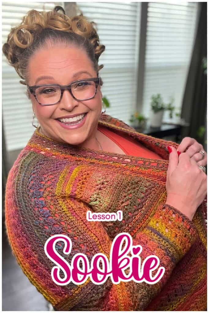 A person with curly hair and glasses smiles at the camera, wearing a colorful knitted shawl with intricate ribbing. Text on the image reads "Lesson 1 Sookie." Bright, natural lighting from windows in the background highlights their knit vest. -Marly Bird