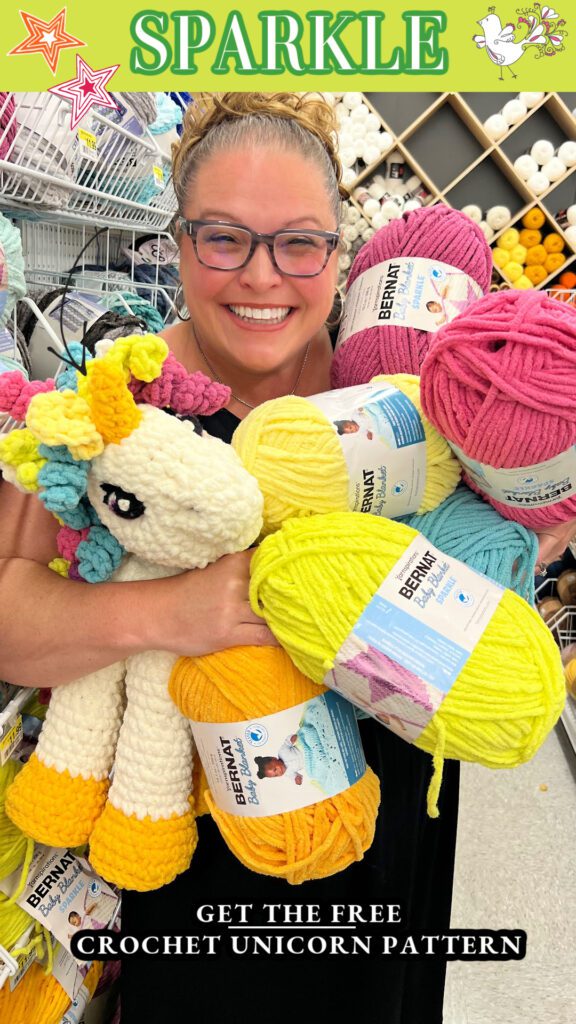 Marly Bird standing in a JOANN store holding all the balls of Bernat Blanket yarn needed to make the crochet unicorn pattern, Sparkles. - Marly Bird