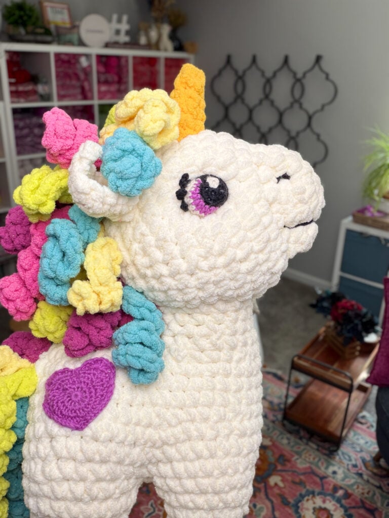 Close-up side profile of Sparkle the Crochet Unicorn showing embroidered eye, gold horn, purple heart cheek, and colorful curly mane — free crochet amigurumi pattern by Marly Bird