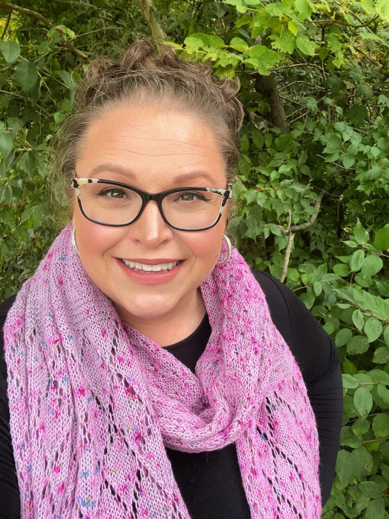 Pink slip stitch knitted scarf with visible texture, worn by a woman outdoors, highlighting stitch detail against green foliage.