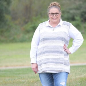 A woman models a gray-and-white striped crochet sweater, showing simple stitch texture and relaxed fit outdoors on grass.