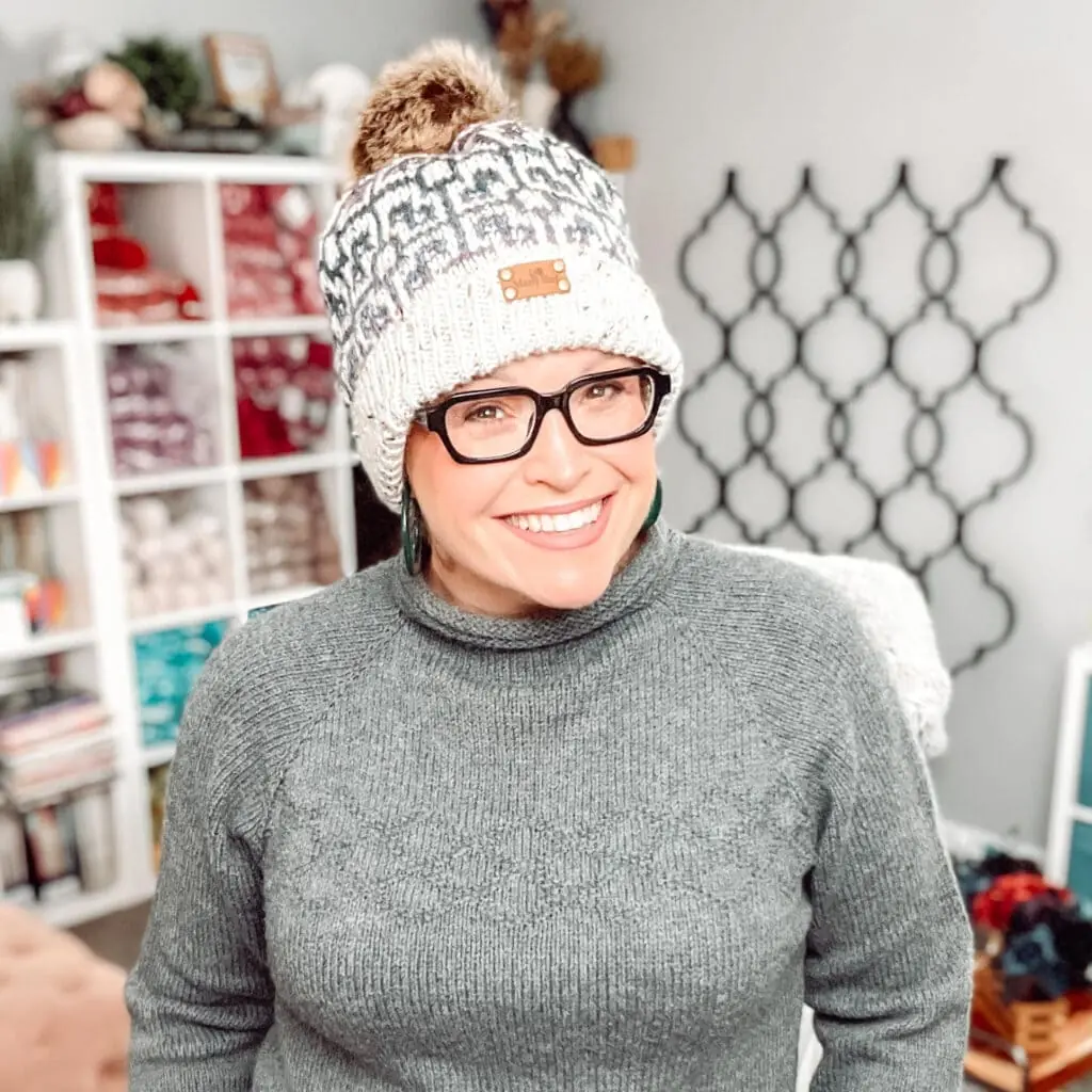 A woman wearing a knit hat and glasses, sporting the cozy style of a Marly Bird Knit Hat Pattern. -Marly Bird