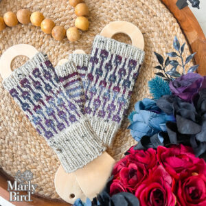 Hand-knitted fingerless gloves in purple and gray, showing detailed textured stitchwork, displayed on wooden blockers.