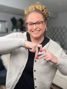 A woman wears a light knit cardigan over a black top, showcasing cozy, textured stitches, and demonstrates hand-finished details.