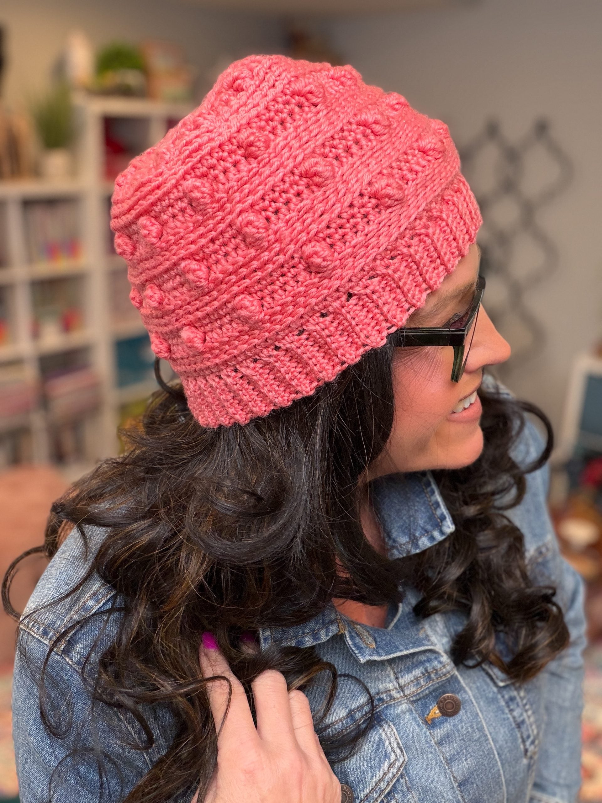 Side profile of Marly Bird wearing a coral Summit Chic crochet hat, showing the raised long double crochet bobble stitch texture across the body of the hat. -Marly Bird
