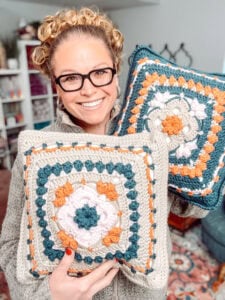 Crocheted pillows with floral granny square patterns in teal, cream, orange, and pink; visible stitch detail and soft texture.