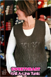 Woman models a brown, sleeveless knit A-line tunic with lace details, standing before yarn shelves. SWEETHEART Knit A-Line Tunic.