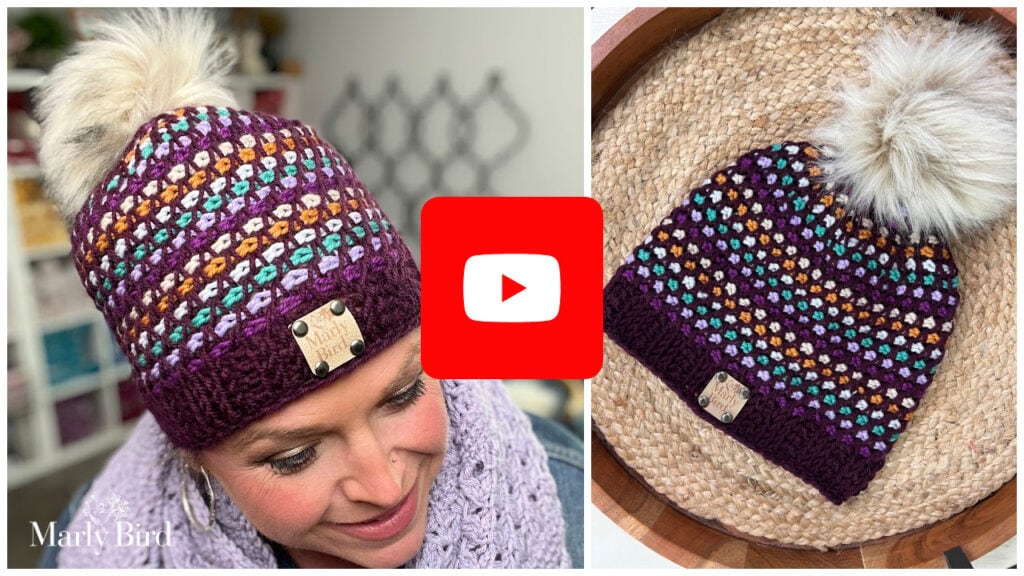 A woman wears a colorful crocheted beanie with a fluffy pom-pom; the beanie, made with Tunisian Crochet, is shown close-up on a woven mat. The YouTube logo overlays the center, suggesting a video tutorial or free hat pattern. -Marly Bird