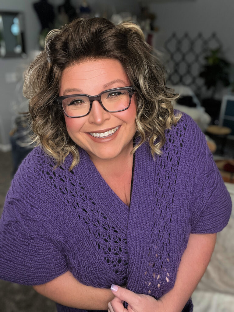 A woman models the Fairhope Cable Knit Cowl sweater, showing off its textured cable stitch and cozy fit in soft indoor lighting.