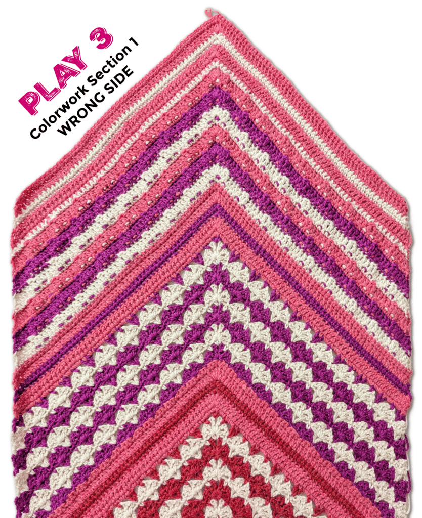 Crochet blanket corner featuring pink, white, and purple stripes with a scalloped stitch pattern, showcasing the wrong side.